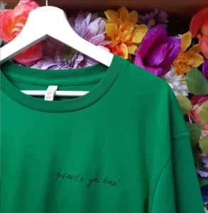 Image shows flower backdrop behind a green Plants Ya Bas' logo shirt