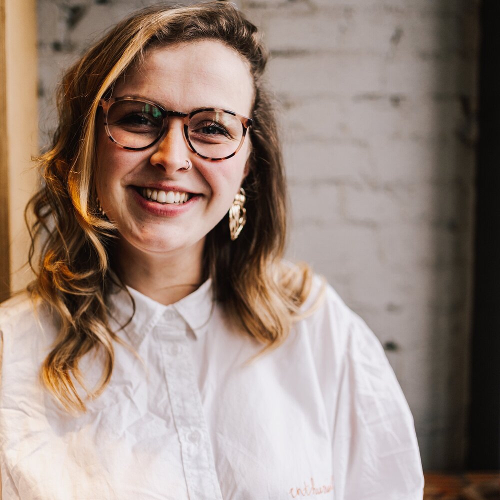 Founder Ellie is seen smiling with Glasses on and big gold earrings 